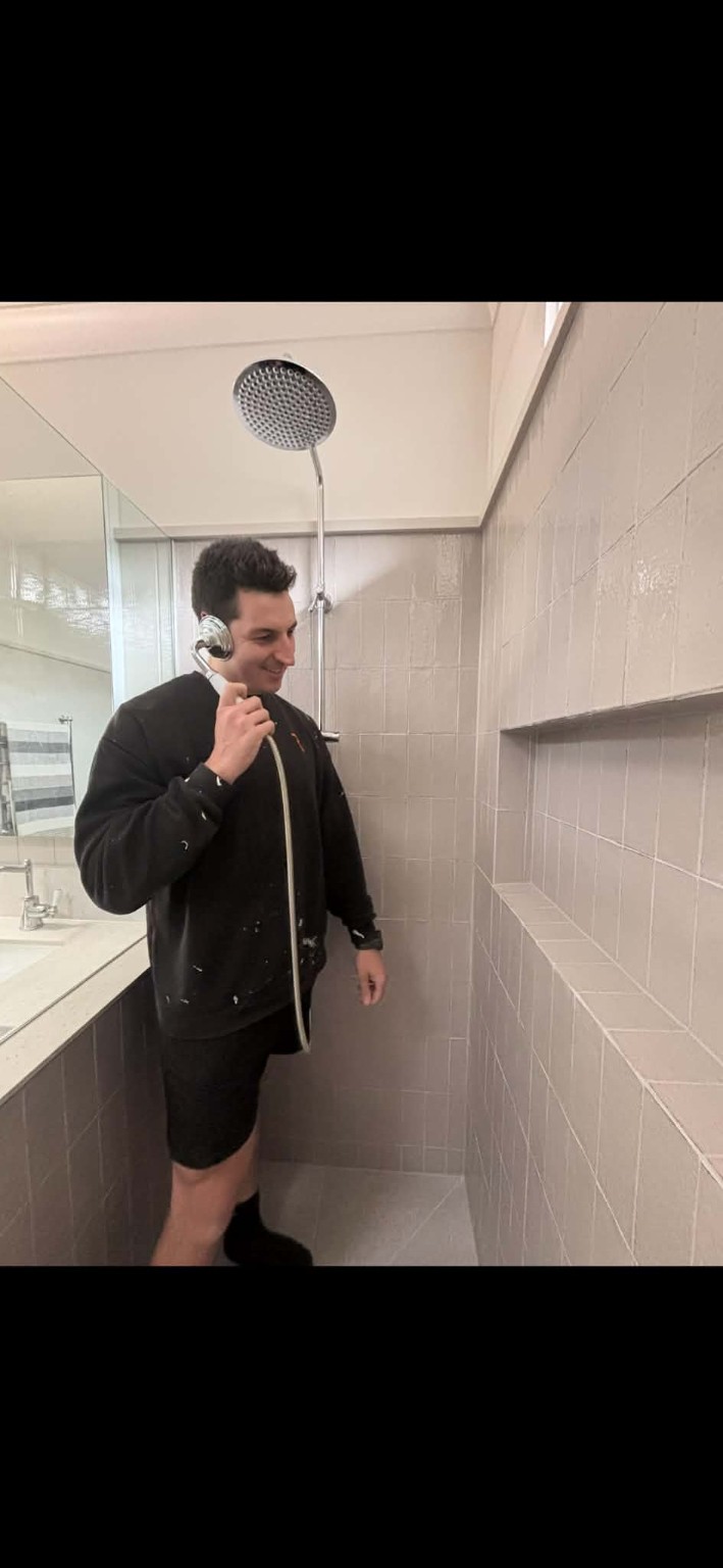 Ray smiling while holding a shower handset like a phone